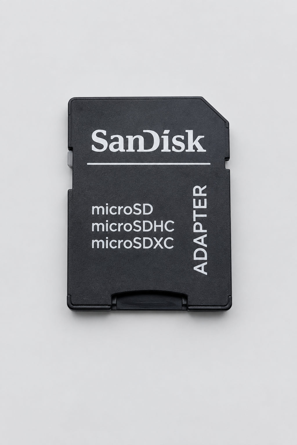 A SanDisk microSD adapter card in black plastic with white printed text, photographed on a light beige textured surface.
